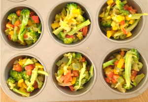 Muffin pan ready to go with an assortment of veggies: broccoli, peppers and pre-cooked onions